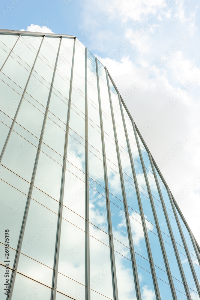 Obraz premium Fragment of a stylish modern high-rise building with a glazed facade which reflects the blue sky and clouds