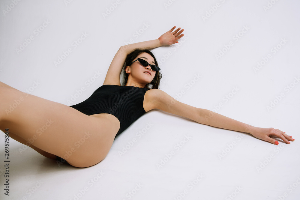 Fashion ballet. Young female ballet dancer in black bodysuit against white studio background. Asian ballerina like a fashion model. Style, contemporary choreography concept. Creative art photo.