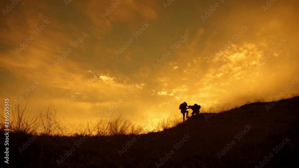 Silhouette of the team on the peak of mountain. Sport and active life of people man and girl. Teamwork couple assistance man and woman hiker, help each other on top of mountain. Silhouette of the team on the peak of mountain. Sport and active life of people man and girl. Teamwork couple assistance man and woman hiker, help each other on top of mountain.