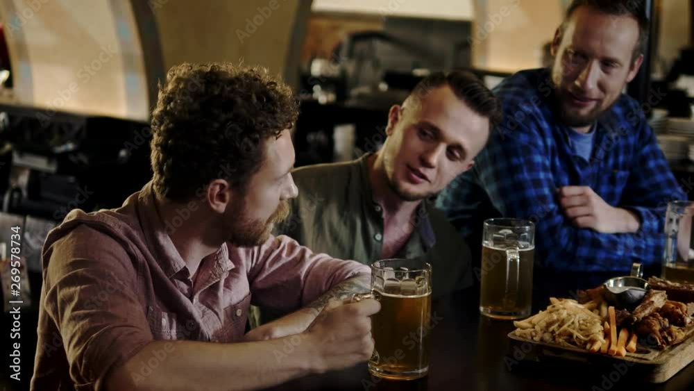 Cheerful friends drinking draft beer and eating snacks in a pub