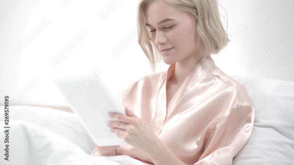 happy blonde girl using digital tablet and smiling in bed happy blonde girl using digital tablet and smiling in bed