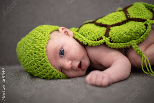 three-month-old baby lying on a sofa and disguised as a green turtle. © Luis