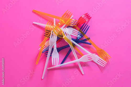 Plastic littering. Ecology problem. Multicolor disposable forks garbage dump over pink background.