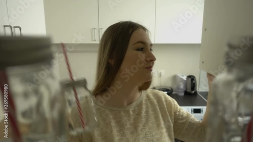 POV of attractive blonde hair young woman opens a cupboard and takes glass from a shelf. Kitchen entourage.