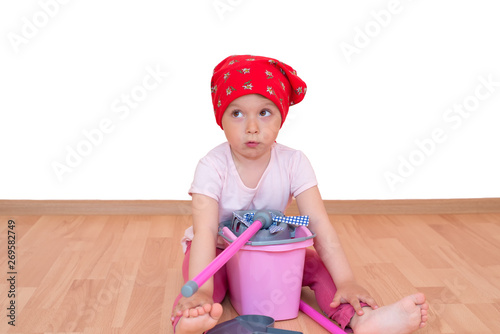 Barefoot little girl with mop and bucket sitting on the floor isolated photo