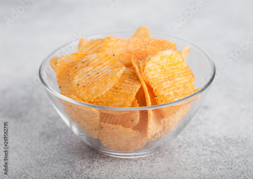Glass bowl plate with potato crisps chips with paprika on light table background.