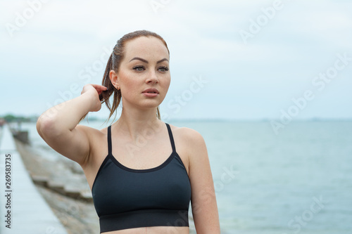 Portrait of a redhead, beautiful, athletic girl with freckles in a black top against the background of the sea, ocean. Outdoor sports