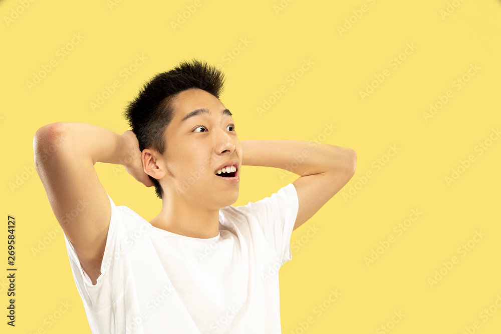 Korean young man's half-length portrait on yellow studio background. Male model in white shirt. Celebrating and happy like a winner or champion. Concept of human emotions, facial expression. Korean young man's half-length portrait on yellow studio background. Male model in white shirt. Celebrating and happy like a winner or champion. Concept of human emotions, facial expression.