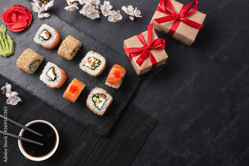 Set of sushi, maki rolls, gift boxes with branch of white flowers on stone table Set of sushi, maki rolls, gift boxes with branch of white flowers on stone table