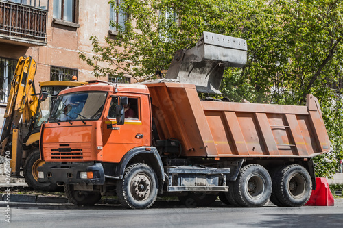 Orange truck and yellow excavator work for repair the asphalt road in a city in summer photo