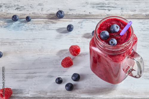 Fresh smoothies with raspberries and blueberries in a glass jar on a wooden white table. Refreshing and healthy summer drink. Copy space, top view