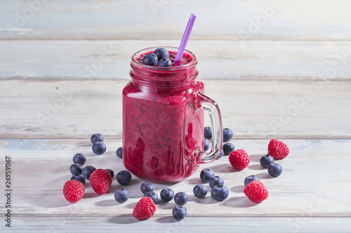 Fresh smoothies with raspberries and blueberries in a glass jar on a wooden white table. Refreshing and healthy summer drink
