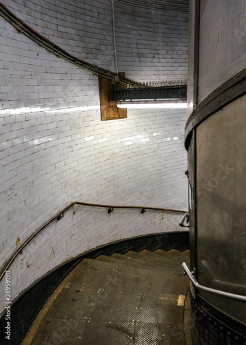 Dark and dirty metal spiral staircase lit by neon light, leading down to Greenwich Foot Tunnel under river Thames in London photo