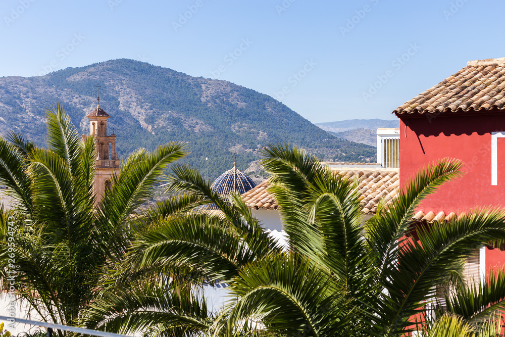 Tiled roofs and dome with ceramic tiles of the church and bell tower and palm trees in the foreground against the backdrop of the mountains, Spain