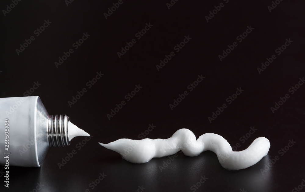 tube of white cream, ointment stroke squeezed out on black background - obrazy, fototapety, plakaty 