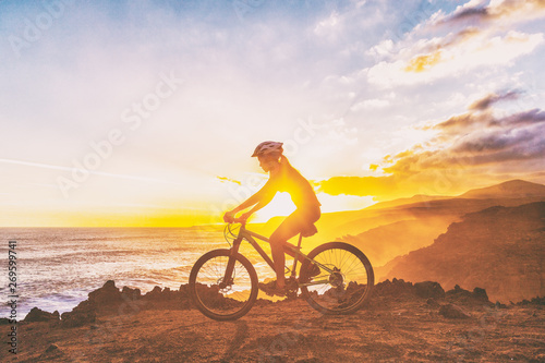 Mountain biking cyclist girl riding MTB bike on coast trail against sunset. Silhouetter of woman doing sports outdoors. Healthy and Active lifestyle.