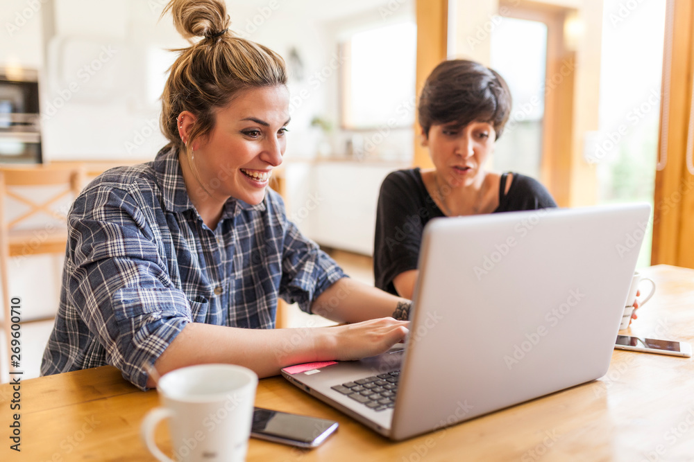 Two beautiful and young women having breakfast at home and using the laptop Two beautiful and young women having breakfast at home and using the laptop