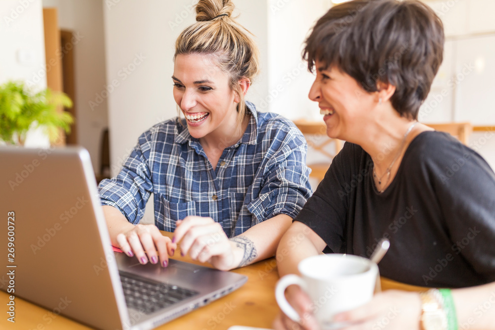 Two beautiful and young women having breakfast at home and using the laptop Two beautiful and young women having breakfast at home and using the laptop