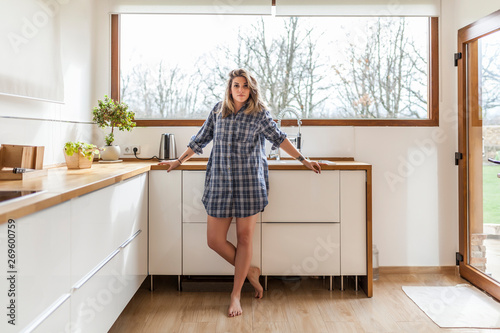 Portrait of blond young woman standing in kitchen at home photo