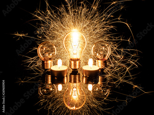 Light bulb with sparklers from behind and candles on black background