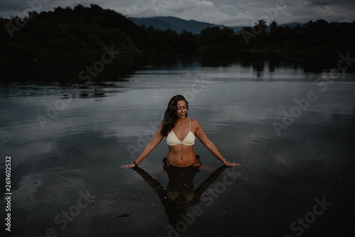 Young woman in swimwear standing in calm water of pond in evening in nature