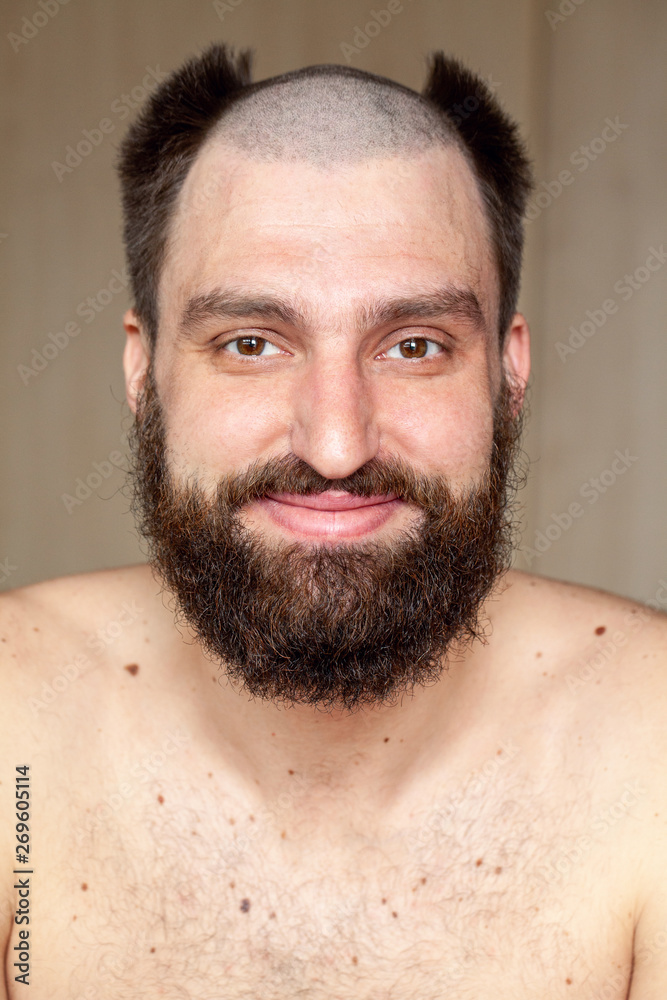 Obraz premium Portrait of man with an unusual hairstyle and beard with a naked torso, looks into the camera 