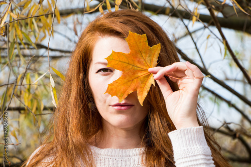 Portrait of young redhead woman with autumn leaf