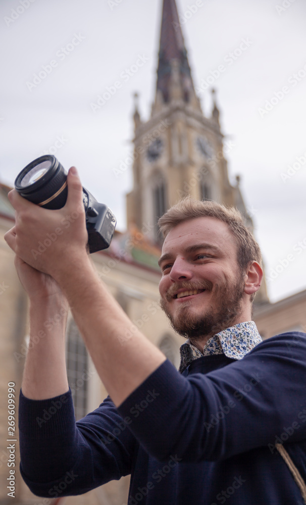 One young man, tourist or traveler using a DSLR camera, in a old European style architecture city behind.