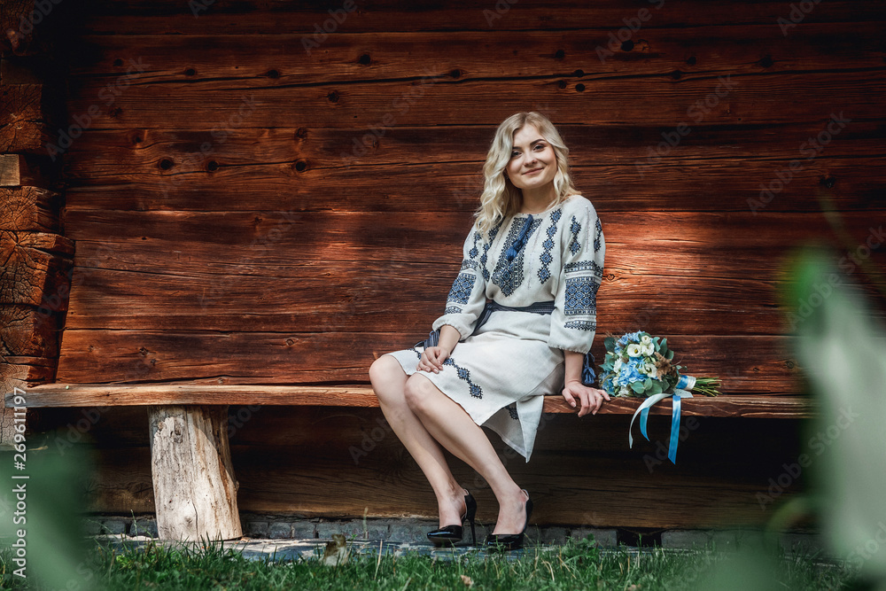 beautiful bride in an embroidered shirt with a bunch of flowers on the background of a wooden house beautiful bride in an embroidered shirt with a bunch of flowers on the background of a wooden house