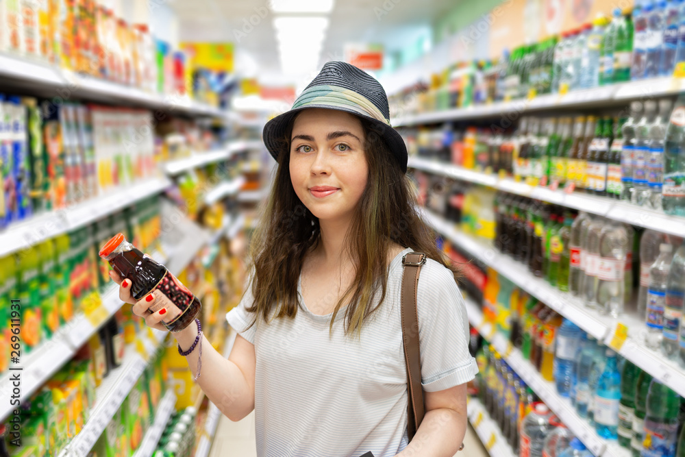 Cute young woman chooses a bottle of juice in the supermarket. Tint