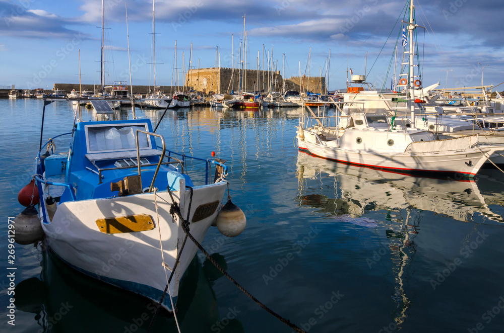 Heraklion, Crete Island - Greece. Fortress Koules (Castello a Mare) at the old Venetian port in Heraklion city. Warm sun light creates reflections of the fortress and the fishing boats on the sea