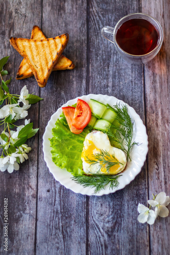 Fried eggs with lettuce, cucumber and tomato slices on wooden background