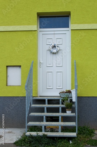 WHITE DOORS OVER STAIRS WITH spring DECORATION.Village scene.Door of a house with spring decoration and green house facade.