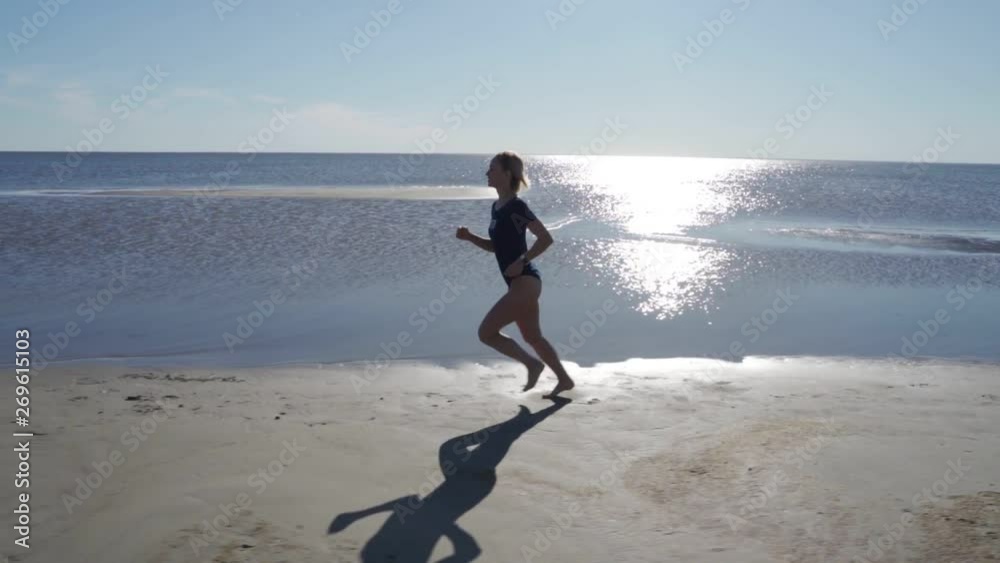 Young woman in swimsuit running on sea beach. Girl jogging along ocean shore. Female tourist having fun. Concept of summer vacation or holiday. Nature landscape with waves at background. Slow motion Young woman in swimsuit running on sea beach. Girl jogging along ocean shore. Female tourist having fun. Concept of summer vacation or holiday. Nature landscape with waves at background. Slow motion