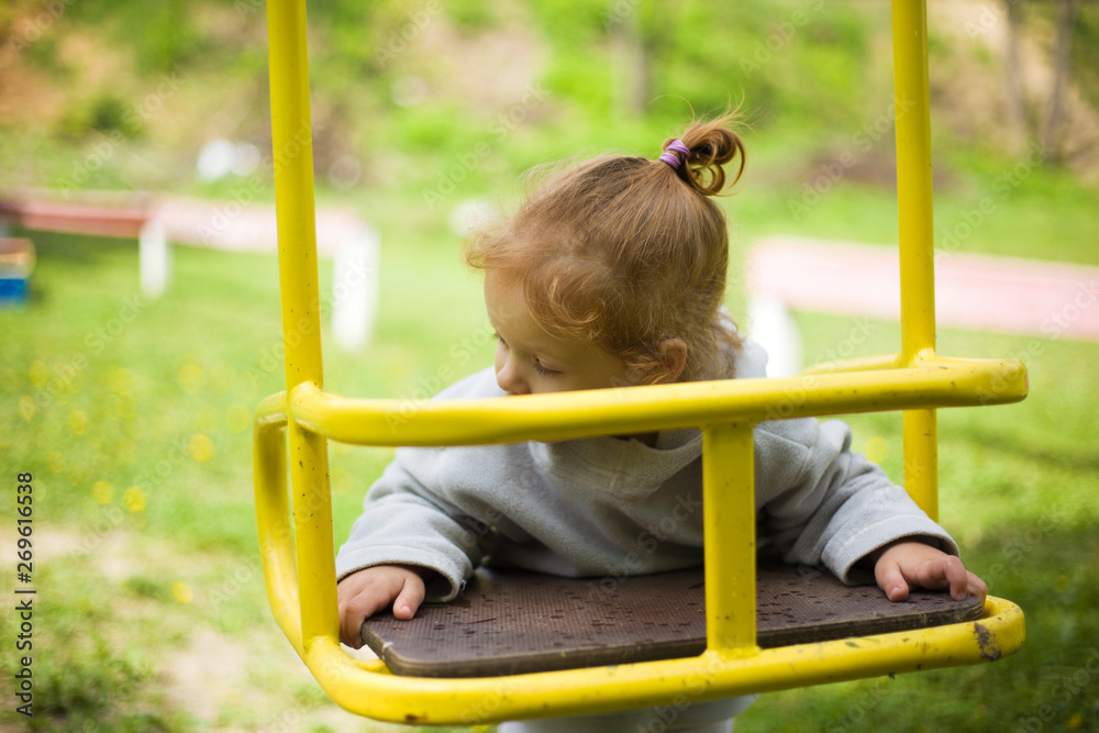 Obraz premium little beautiful red-haired girl hung on a swing, baby plays on a swing on the playground