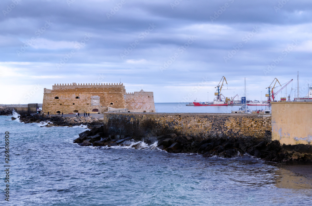 Fortress Koules, Crete - Greece. Fortress Koules (Castello a Mare) at the old Venetian port in Heraklion city at sunset time with cloudy sky. Big cranes visible in the background