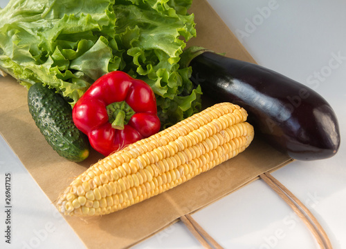 Paper bag full of fresh vegetables on light background. Sweet pepper  cucumbers  corn  salad  eggplant. Top view