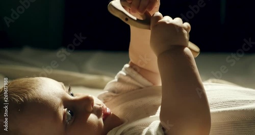 Close-up of adorable curious baby playing with wooden toy in the bed. Little baby playing with wooden toys at night in dark room