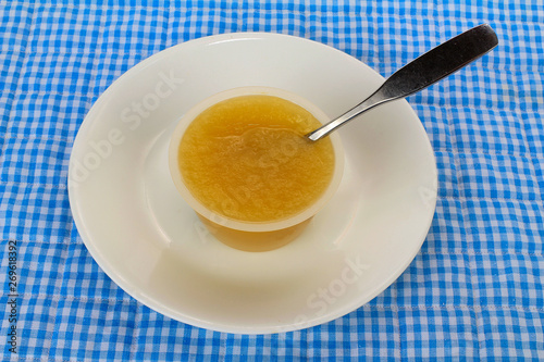 Small plastic cup of apple sauce on white plate against blue gingham background.