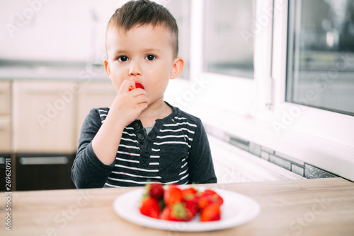 Little boy in the kitchen eating fresh strawberries very appetizing