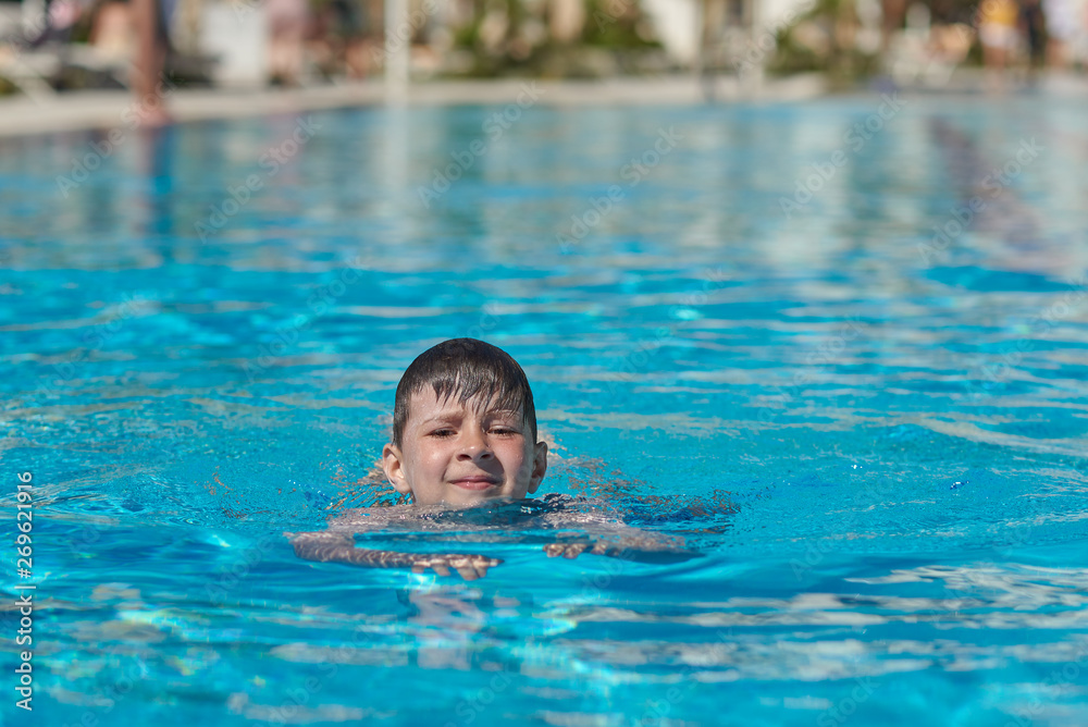 Portrait of cheerful European boy swimming in pool, he is enjoying his summer vacations.