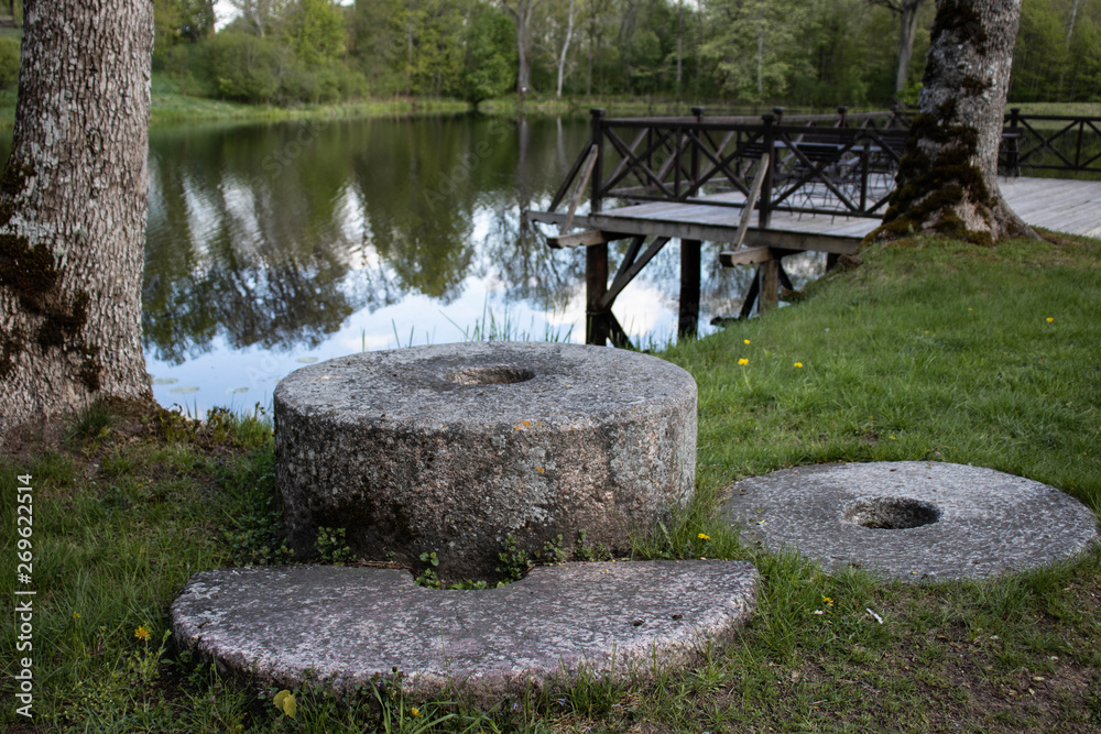 Old millstones lie on the grass near the river and wooden platforms. Old millstones lie on the grass near the river and wooden platforms.