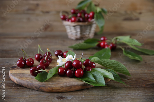 fresh organic cherries in a wicker basket with leaves and white flowers on the wooden rustic background. Healthy food concept. Copy space.