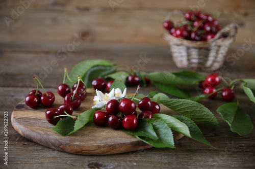  Fresh organic cherries on a branch with green leaves with cherries in a wicker basket with green leaves and white flowers on a wooden rustic background. The concept of healthy eating. With copy space