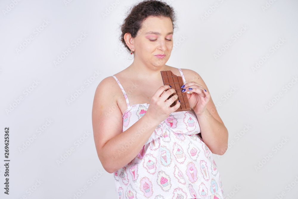 curvy woman in funny pajamas with a chocolate bar stands on a white background in the Studio