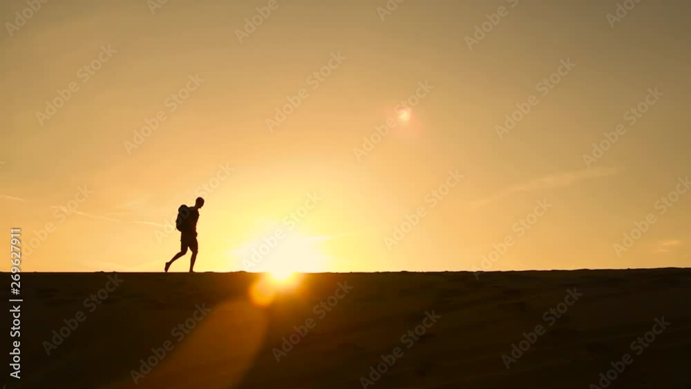 Traveler with a backpack goes through the desert. Silhouette at sunset Traveler with a backpack goes through the desert. Silhouette at sunset