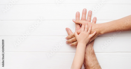 Hands of father, mother and kid on white wooden background