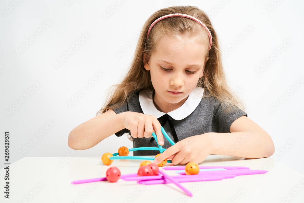 Little girl photographed against white background wearing school uniform dress isolated trying to solve geometric puzzle Little girl photographed against white background wearing school uniform dress isolated trying to solve geometric puzzle