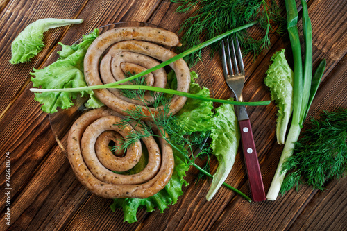 Grilled pork sausages lie on a wooden table with greens: lettuce, dill, parsley and onion. View from above. Picnic - barbecue