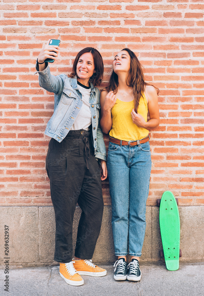 Young women couple making a selfie. Behind brick wall. Positive emotion and tolerance concept.